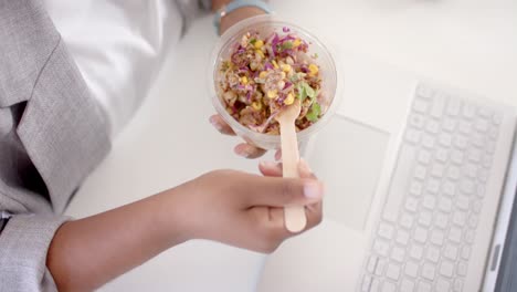 primer plano de una mujer de negocios afroamericana casual almorzando usando una computadora portátil en la oficina, cámara lenta