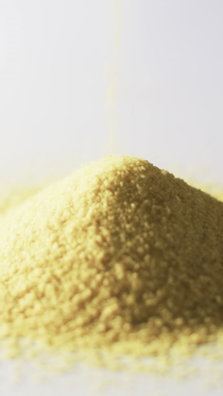 Vertical video of close up of heap of yellow sand grains and copy space on white background