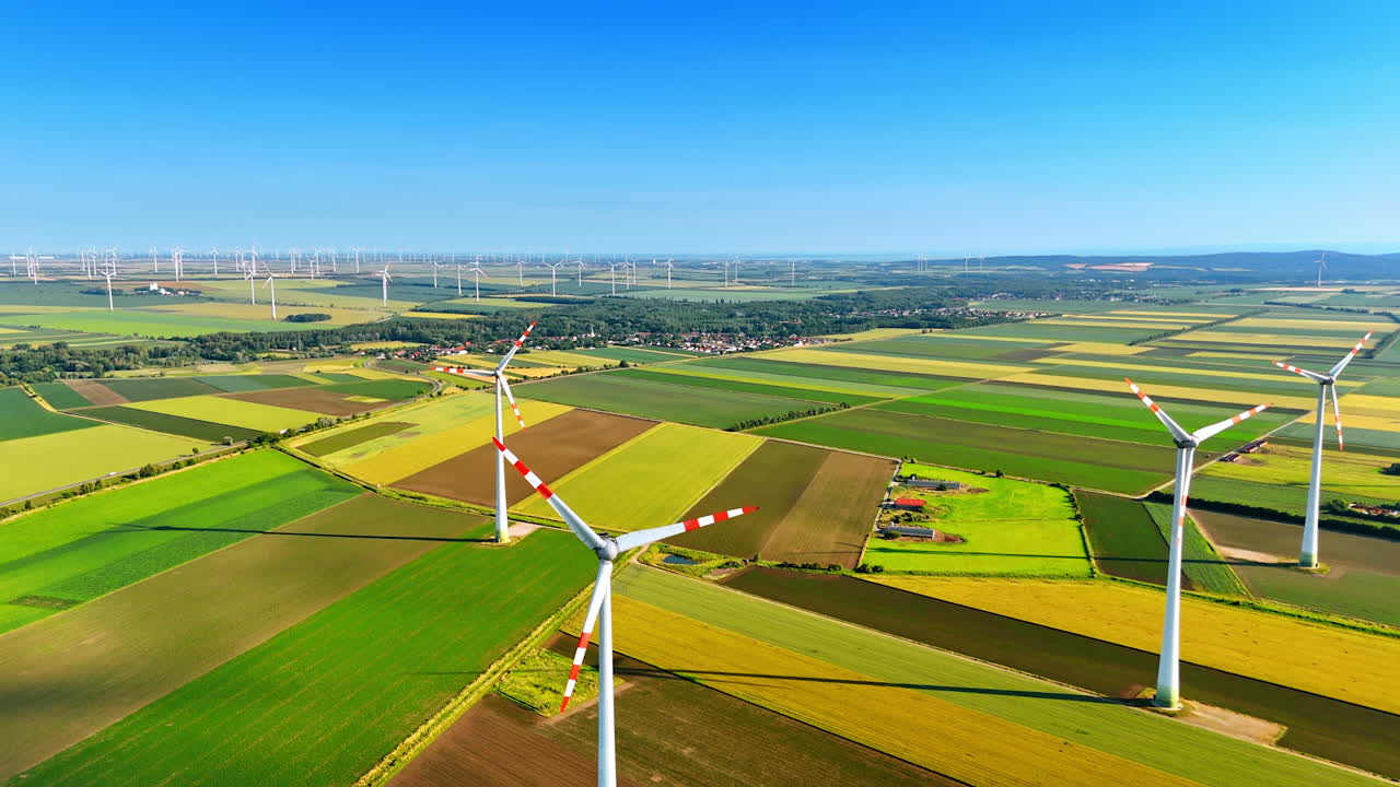 Tall wind turbines on farms. Vast green and gold landscapes under a clear blue sky feature tall wind turbines producing energy