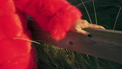 woman in vivid red fur coat strolling along beach walkway at dusk - detail close up