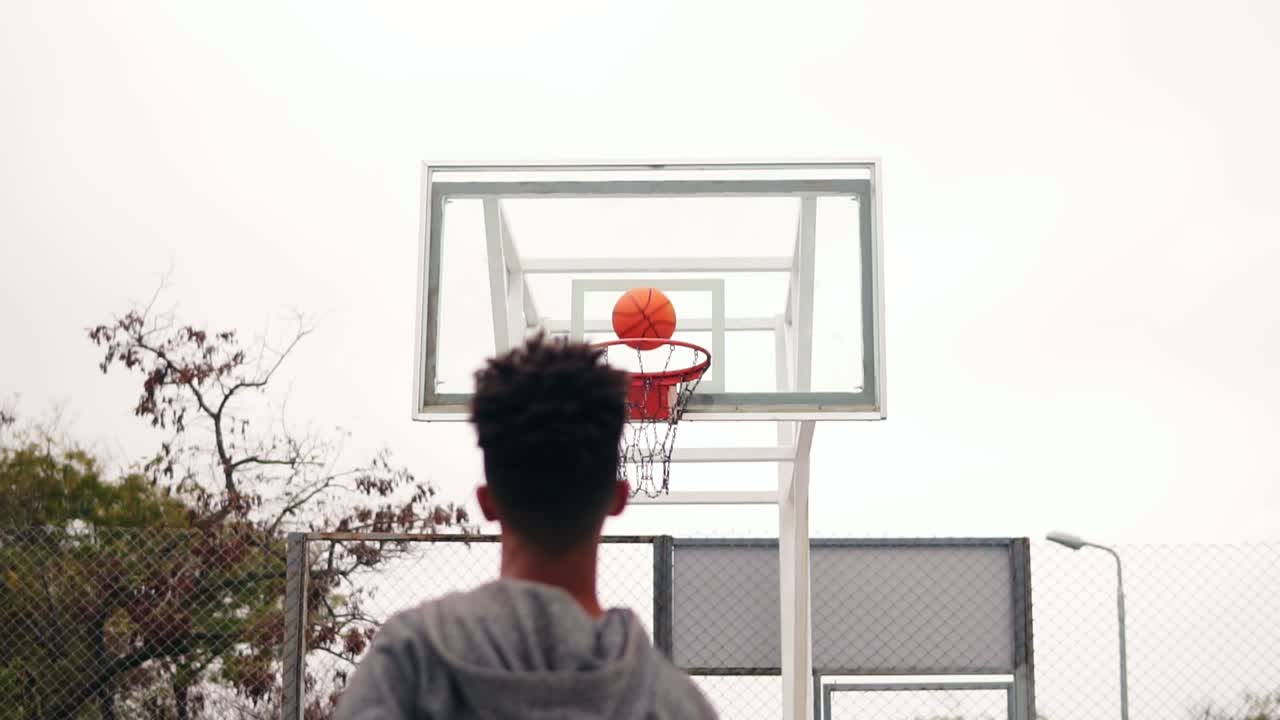 vista de atrás de un jugador africano irreconocible saltando y lanzando la pelota en un aro de baloncesto, la pelota golpea el anillo y anota