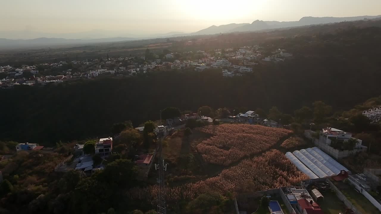 Warm sunset illuminating houses, crops and mountains in Cuernavaca, Mexico, offering a breathtaking aerial view of the cityscape and surrounding landscape, drone reveal