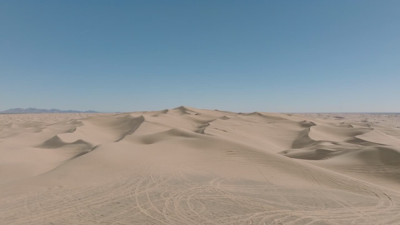 un dron voló hacia atrás sobre las dunas del desierto, el cielo azul por delante y los picos arenosos por debajo