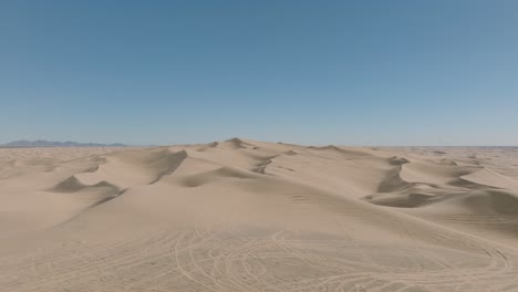 Drohnenschuss,-Der-Rückwärts-über-Wüstendünen-Fliegt,-Blauer-Himmel-Voraus-Und-Sandige-Gipfel-Darunter