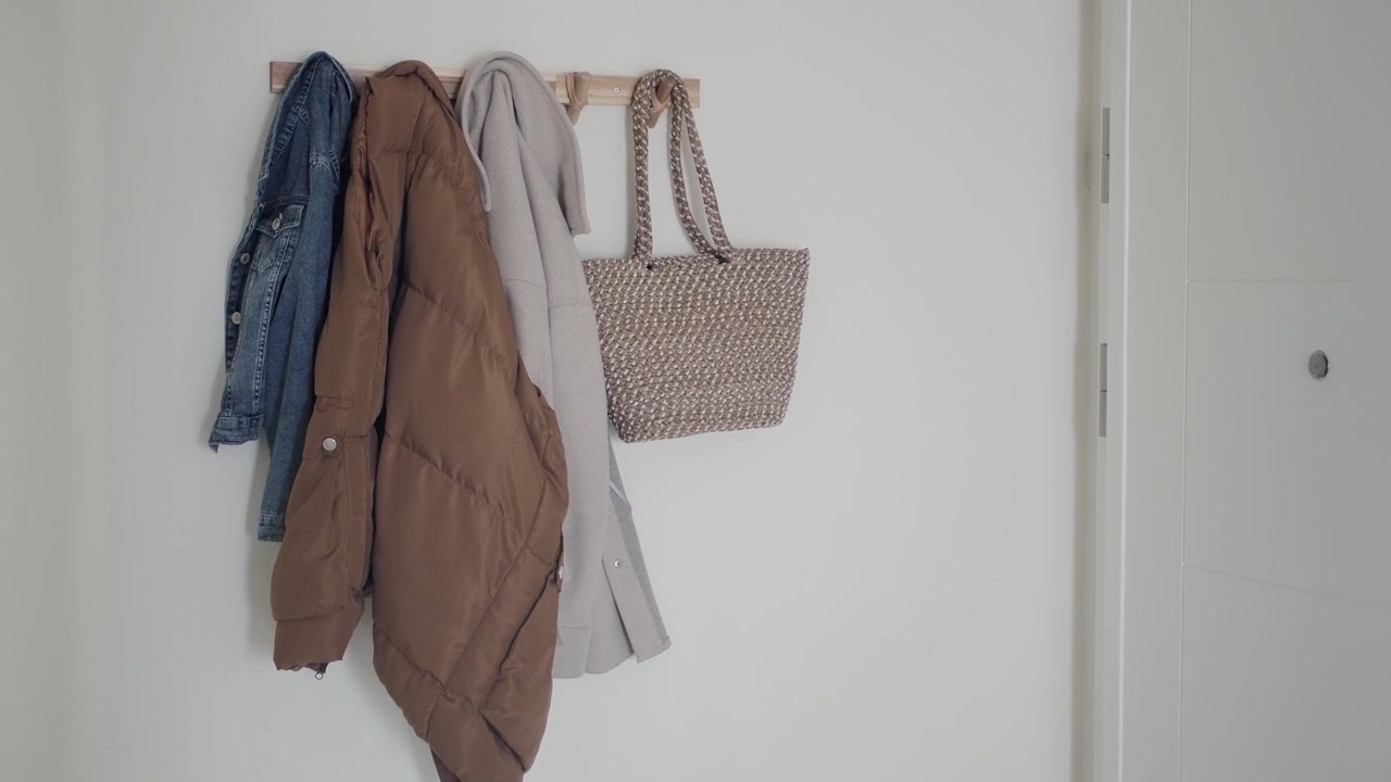 Vari cappotti e una borsa tote intrecciata appesi a un gancio a muro