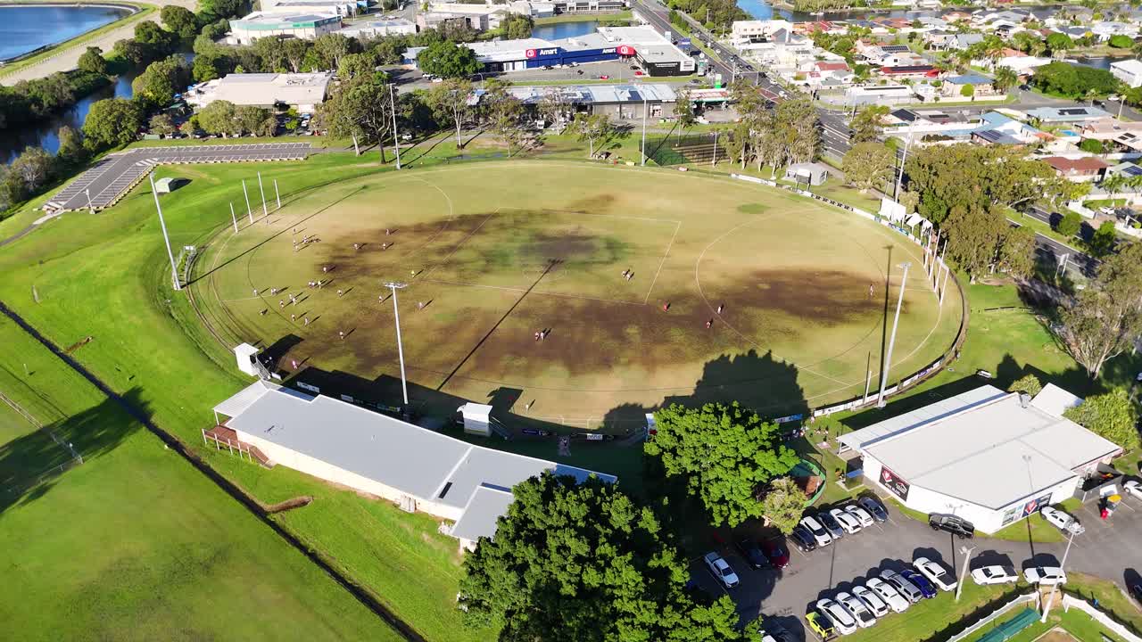 Drone footage captures a sunny day over an Australian football oval in Gold Coast, highlighting the field and surrounding area