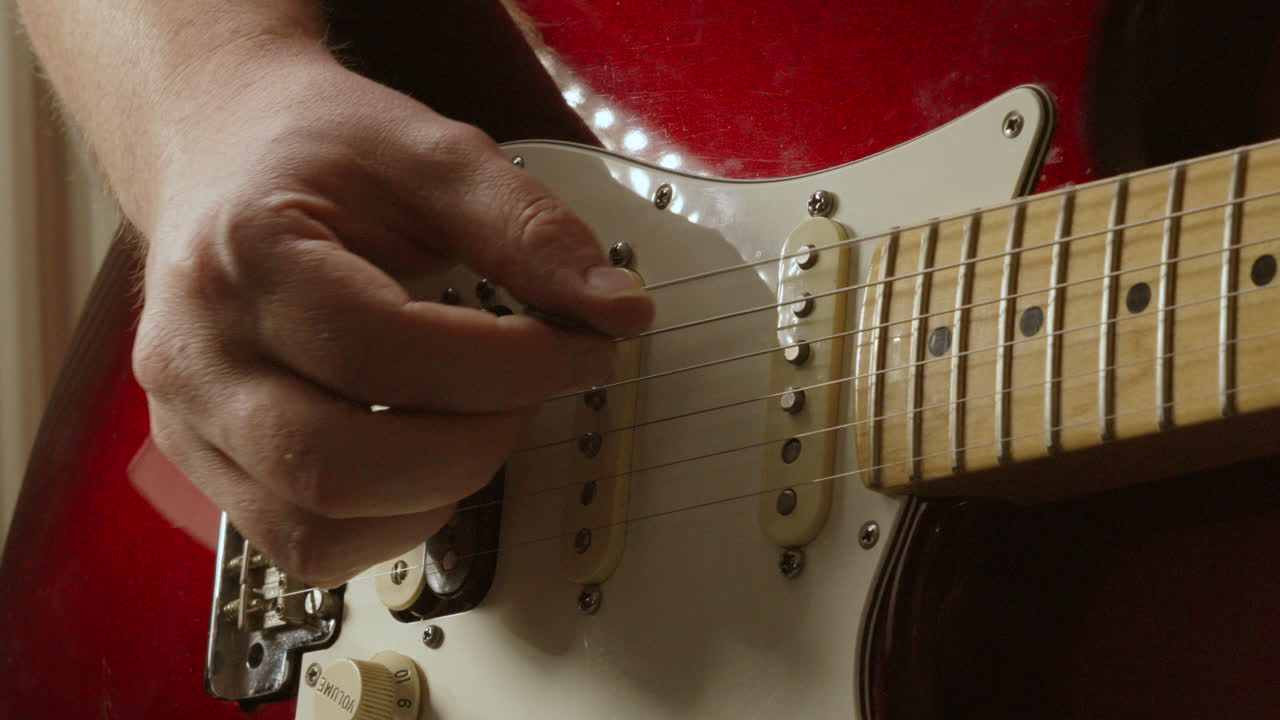 guitarrista arrancando suavemente las cuerdas con plectrum en la guitarra stratocaster roja en cámara lenta en un entorno de iluminación natural 4k