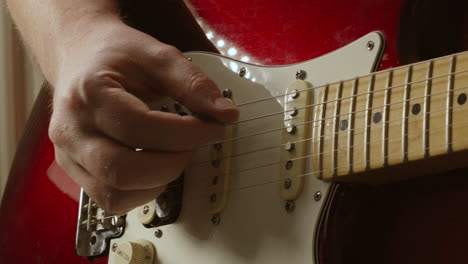 guitarist gently plucking strings with plectrum on red stratocaster guitar in slow motion in natural lighting environment 4k