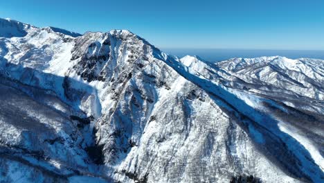 Aerial-wide-establishing-tracking-shot-of-Japan's-mount-myōkō,-on-a-clear-winter-day,-a-volcanic-mountain-in-Myoko-Togakushi-Renzan-National-Park-region