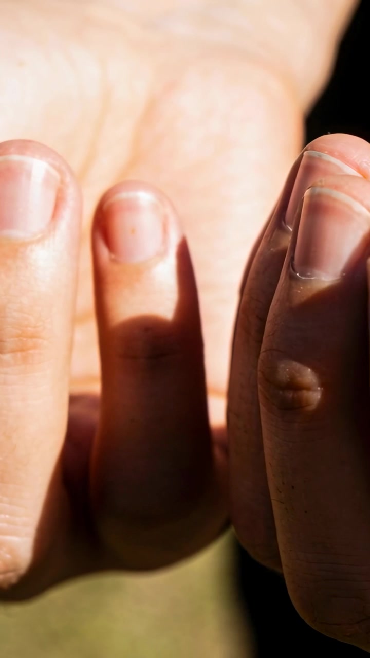 Vertical video: Moving adult hands tilting fingers in studio as cam rolls, shifting nail highlights