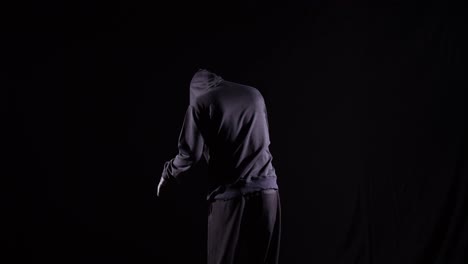 scary man in the hooded sweatshirt wearing halloween mask stabbing with a knife and turning to camera making threatening gesture on the black background