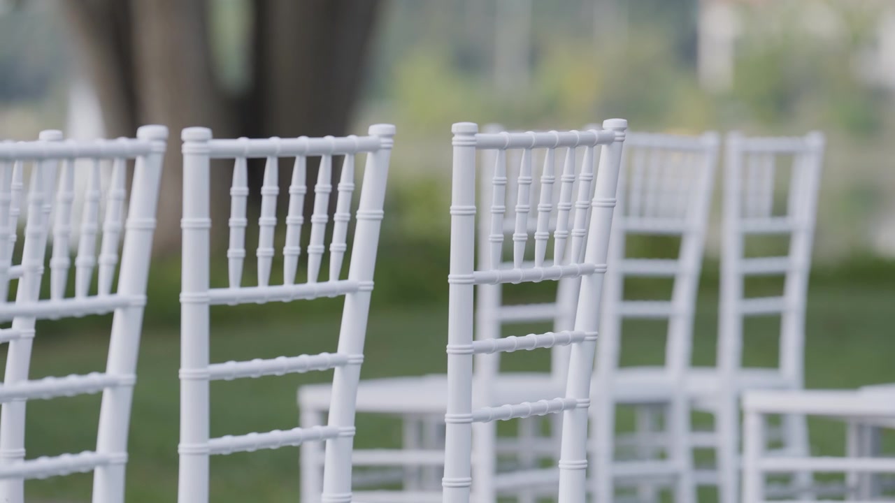 event planner organise move white chair in outdoor location with park garden tree in blurred background