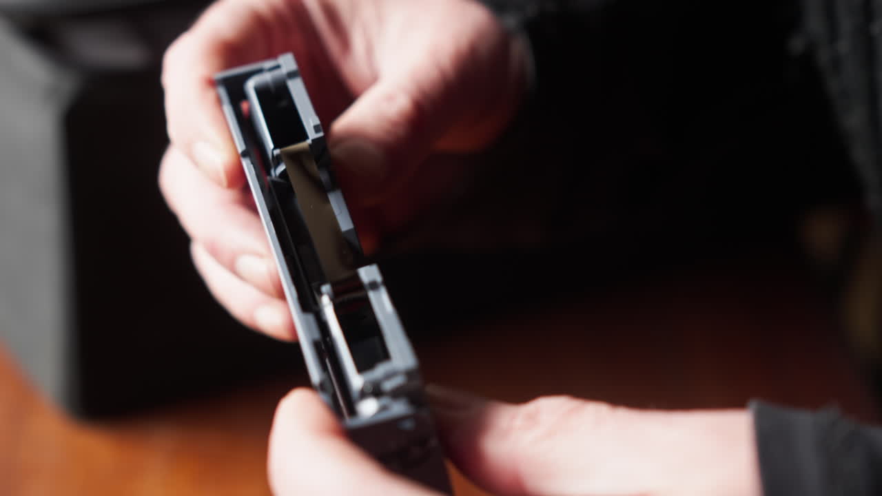 Makro close-up tangan yang memeriksa kaset video magnetik, menyiratkan penyelidikan, tinjauan arsip, atau penemuan kembali kenangan yang terekam.
