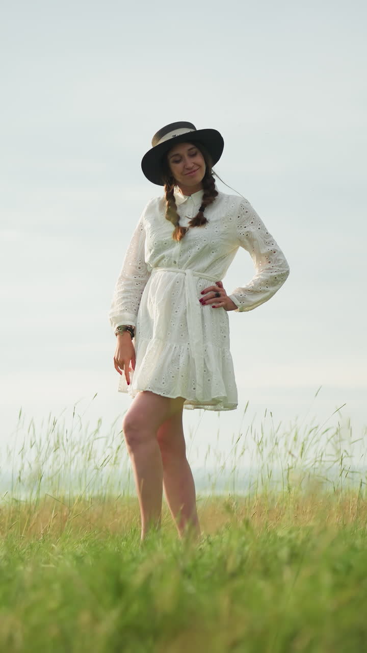 una mujer con un vestido blanco y sombrero posa con gracia en un campo de hierba serena como un artista invisible en una camisa a cuadros y vaqueros pinta su retrato en un lienzo grande