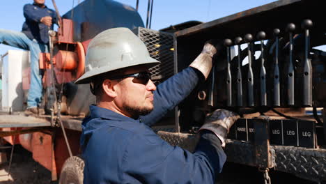 man in blue uniform shirt and white helmet touching the lever of drilling equipment. close up. people operating the machinery at gas production site.
