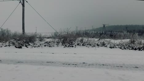 POV-Des-Autoreisepassagiers,-Der-Straßenrandlandschaft-Durch-Schmutziges-Fenster-Betrachtet-Winterlandschaftsschneewald-Kahle-Bäume-Bahntraktion-Bewölkter-Himmel