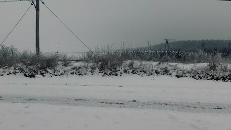 punto de vista del pasajero del viaje en automóvil mirando el paisaje al borde de la carretera a través de la ventana sucia paisaje invernal bosque nevado árboles desnudos tracción ferroviaria cielo nublado