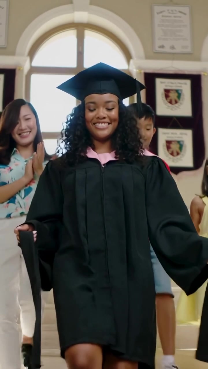 Vertical video: Cue sending graduate in gown and cap down hall steps with family, showing tassel