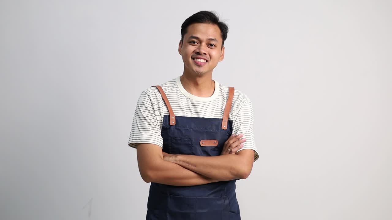 Pria Asia muda merapikan celemeknya bersiap-siap untuk bekerja, tampan dan percaya diri dengan tangan terlipat