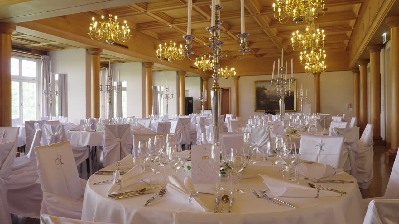 Luxury wedding reception hall with round tables, chandeliers and white decor – wide interior shot