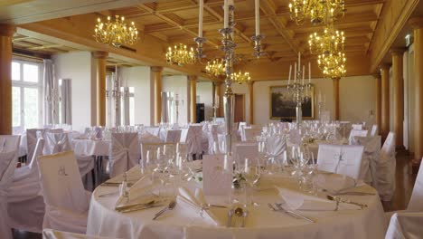 luxury wedding reception hall with round tables, chandeliers and white decor – wide interior shot