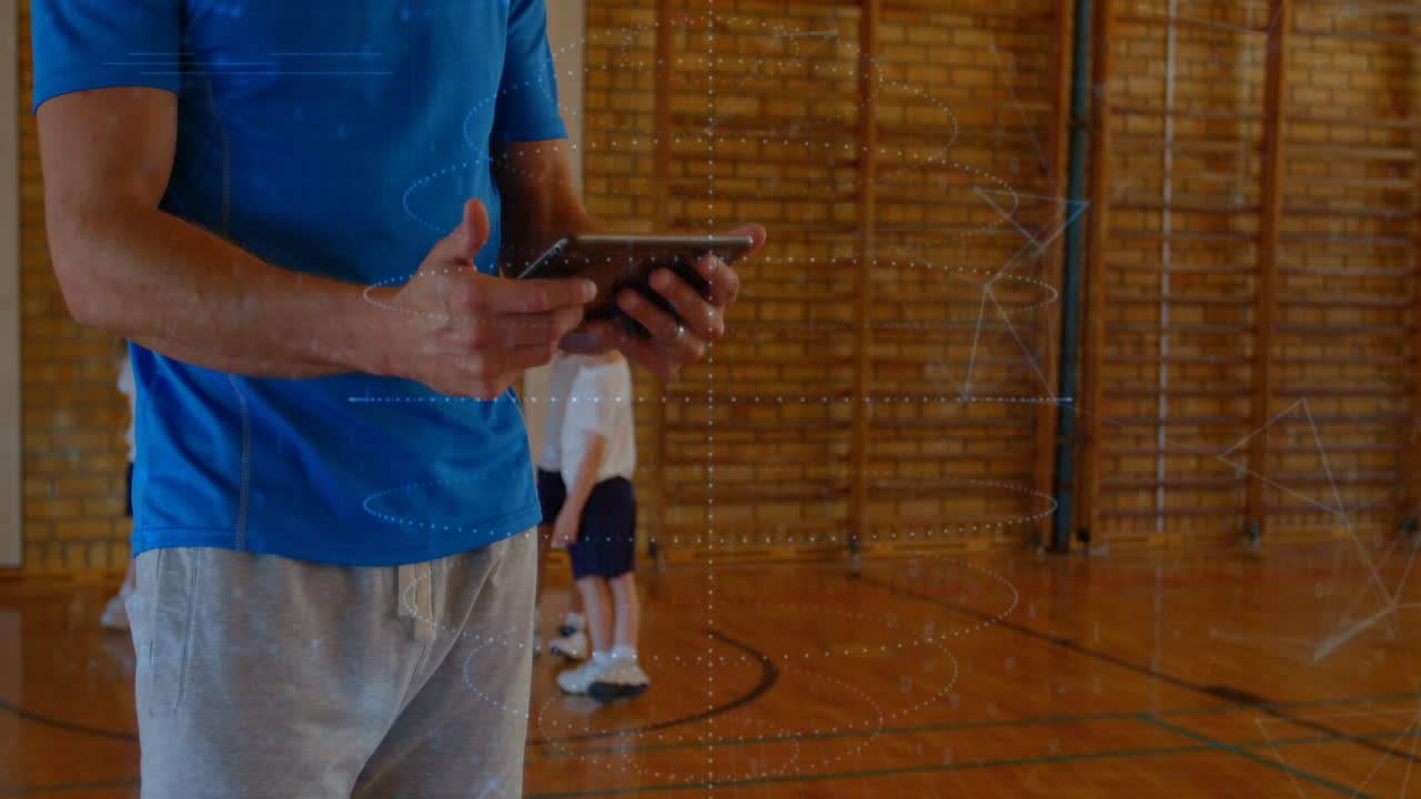 Coach tapping tablet and supervising boys in school gym, digital overlay over tablet analyzing data