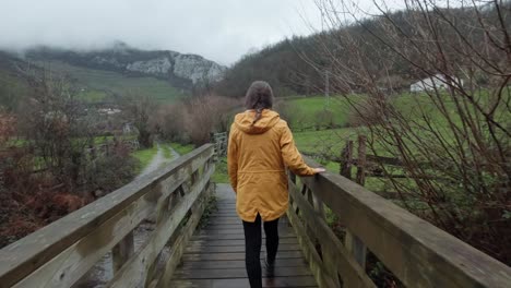 woman in yellow coat walking on bridge in asturias, spain