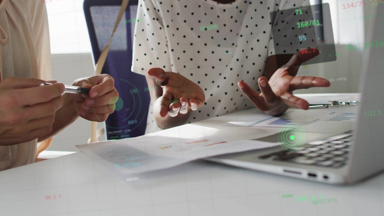 Two women reviewing charts in business, right tapping sheet after pointing, green overlays marking