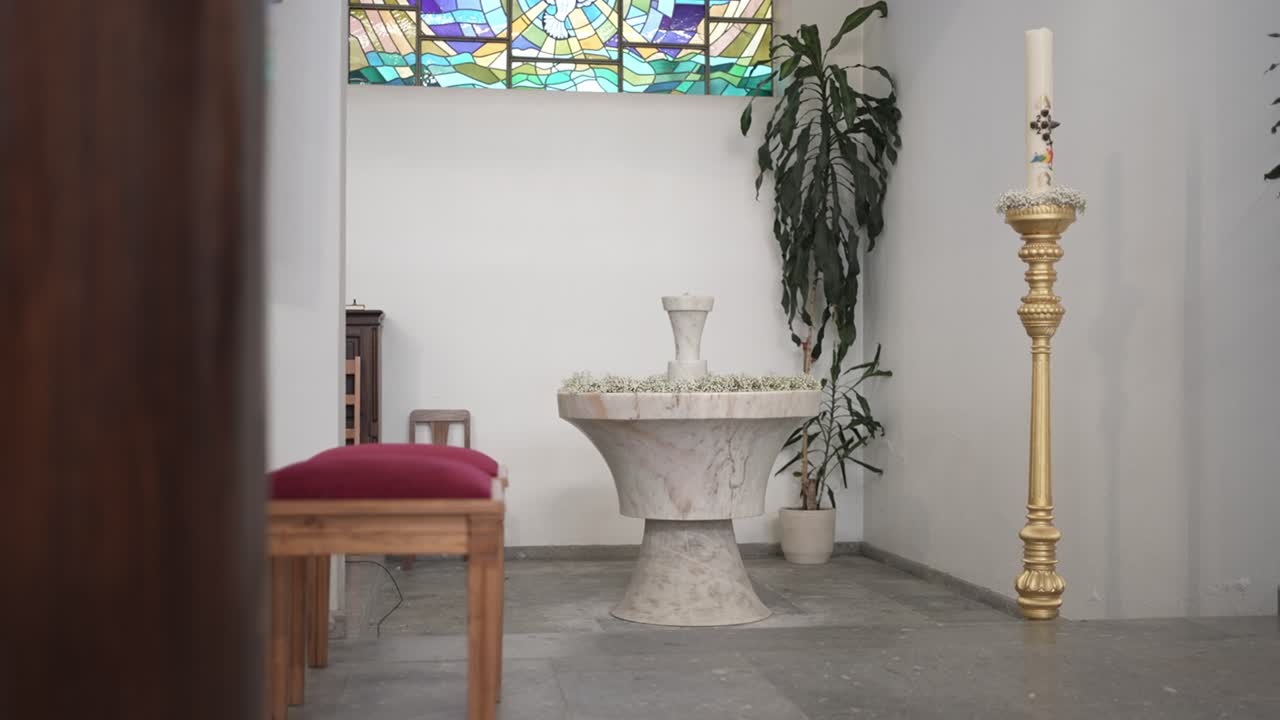 고요한 예배당에 있는 금빛 양초와 스테인드글라스가 있는 대리석 세례반
