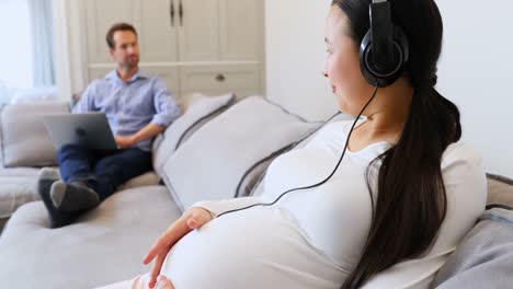 pregnant woman listening to music on headphones in living room 4k