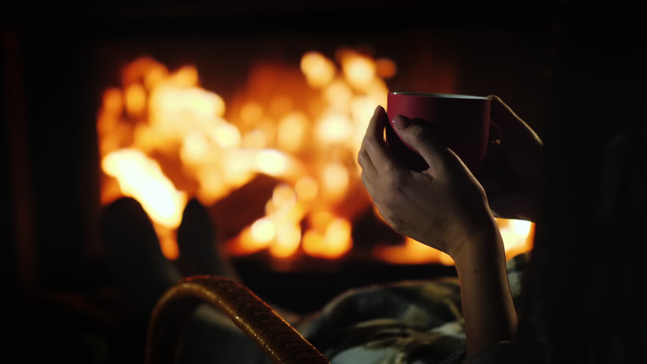 벽난로 옆의 차 - 벽난로 뒤에 빨간 컵이 있는 여성의 손