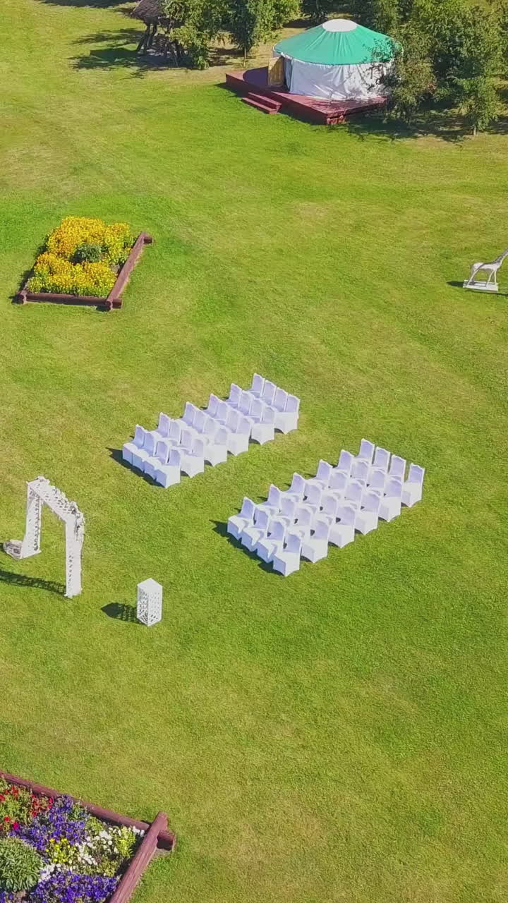green site with different decorations prepared for wedding ceremony near tranquil lake on sunny autumn day bird eye view