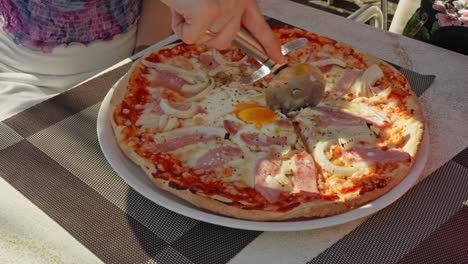 Woman-slicing-a-freshly-baked-ham-and-cheese-pizza-using-handheld-roller-blade-cutter,-static