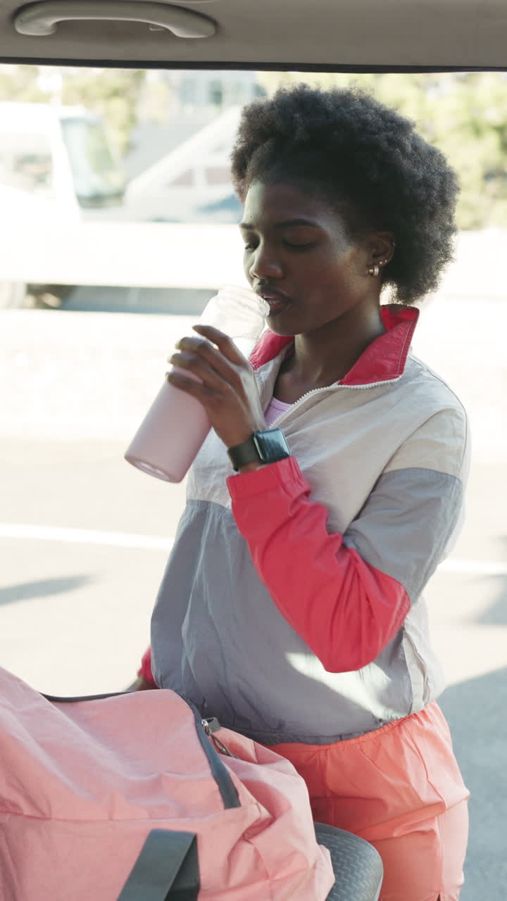 Giovane donna di colore che beve acqua e controlla lo smartwatch all'aperto