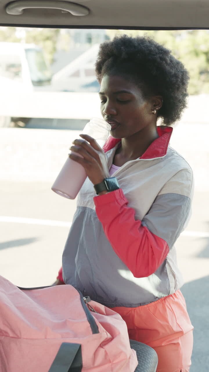 Giovane donna di colore che beve acqua e controlla lo smartwatch all'aperto