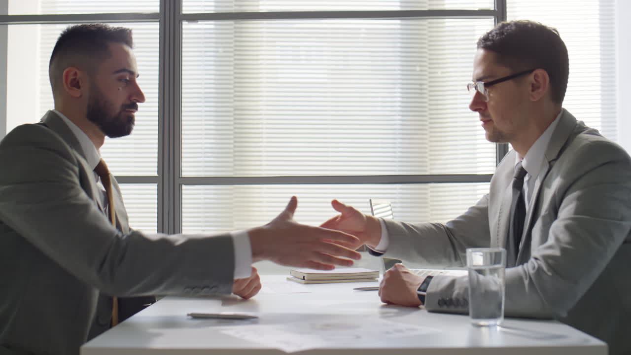 Two Businessmen Speaking and Shaking Hands in Office