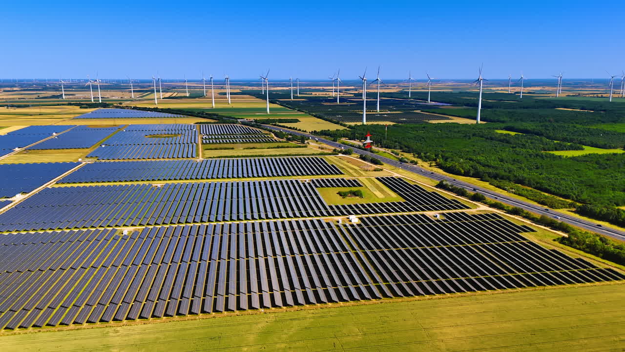 Highway crosses the vast nature landscape in the countryside. Aerial perspective on the solar panels site and wind farms