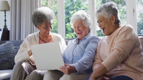 Three-diverse-senior-women-using-laptop-together-sitting-on-the-couch-at-at-home