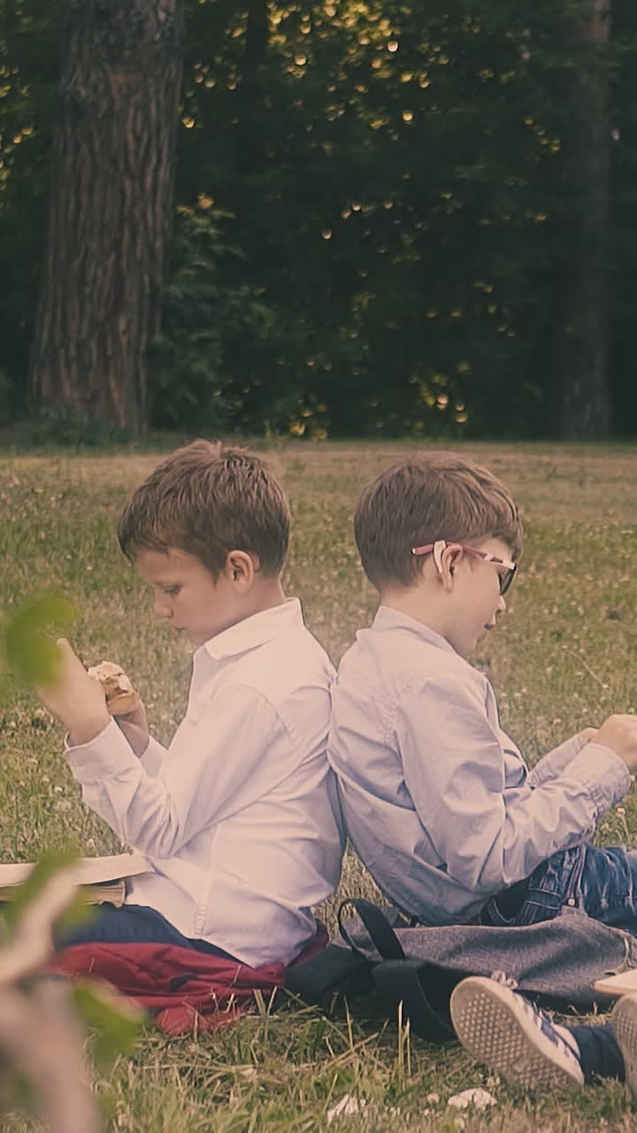 junior schoolboy eats sandwich sitting near classmate and small writing girl in school yard close view slow motion