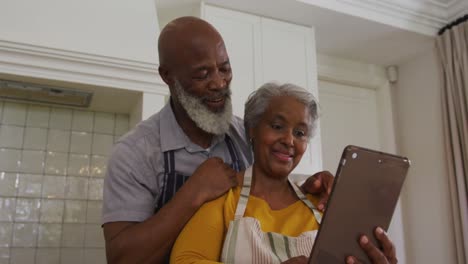 Pareja-De-Ancianos-Afroamericanos-Haciendo-Una-Videollamada-En-Una-Tableta-Digital-En-La-Cocina-De-Casa