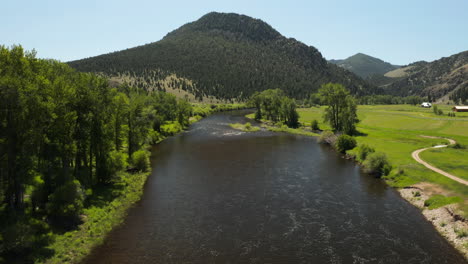 river flowing through green sunny landscape with mountains, drone