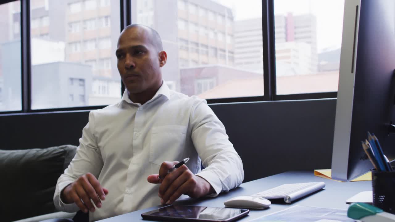 uomo d'affari di razza mista seduto usando il computer sfregando il mento in un ufficio moderno