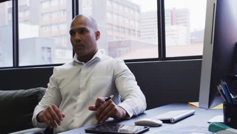 mixed race businessman sitting using computer rubbing chin in modern office