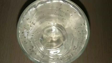 slow motion and close up of water dripping drop by drop in a glass container filled with clear water and spilling over