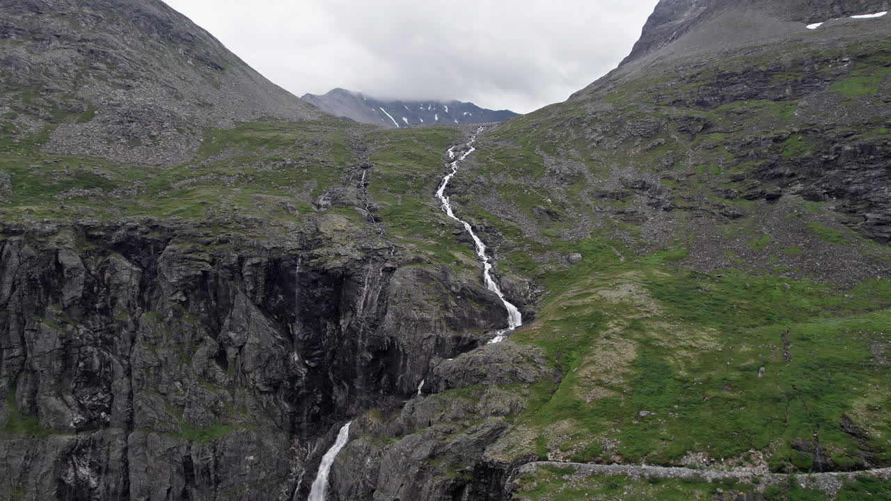 amplia toma aérea de dolly, empujando lentamente en un río largo, delgado y corriente, serpenteando por una empinada ladera cubierta de musgo por trollstigen, noruega