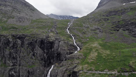 wide aerial dolly shot, pushing in slowly on a long, thin, rushing river, winding down a steep, mossy hillside by trollstigen, norway