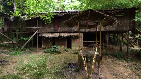 A traditional elevated house with a thatched roof stands among tropical plants in Mari Mari cultural village, Kota Kinabalu, Malaysia - pan reveal