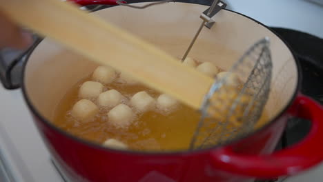 moving doughnut holes deep frying in oil with wire strainer, slow motion