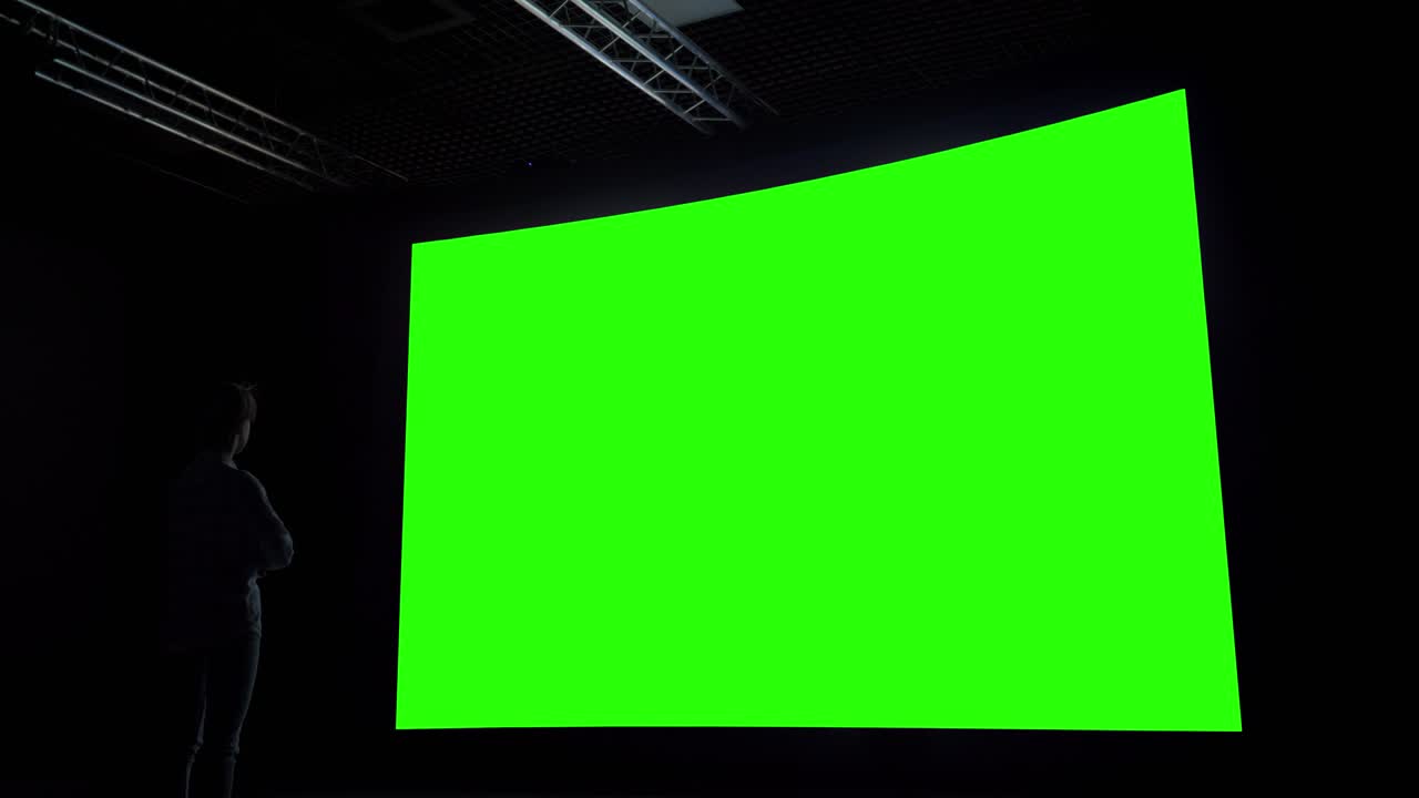 Woman looking at large blank green screen in dark room - chroma key concept