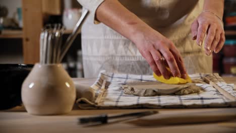 young woman potter wetting the clay using a sponge